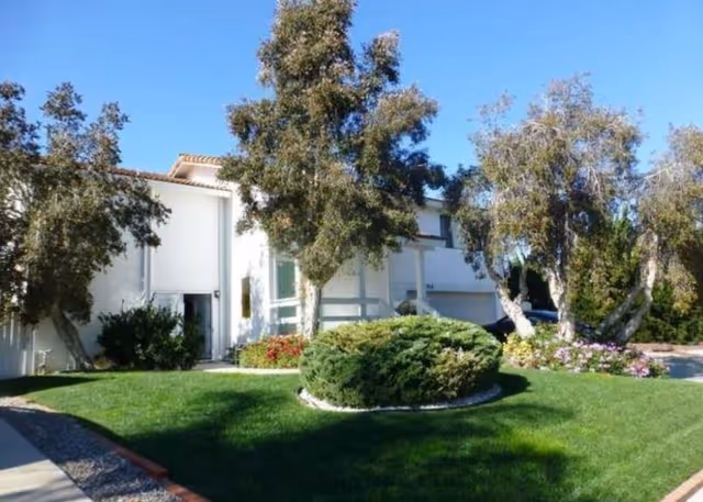 La Costa Villas exterior showcases a white building with manicured lawn, trees, and shrubs.