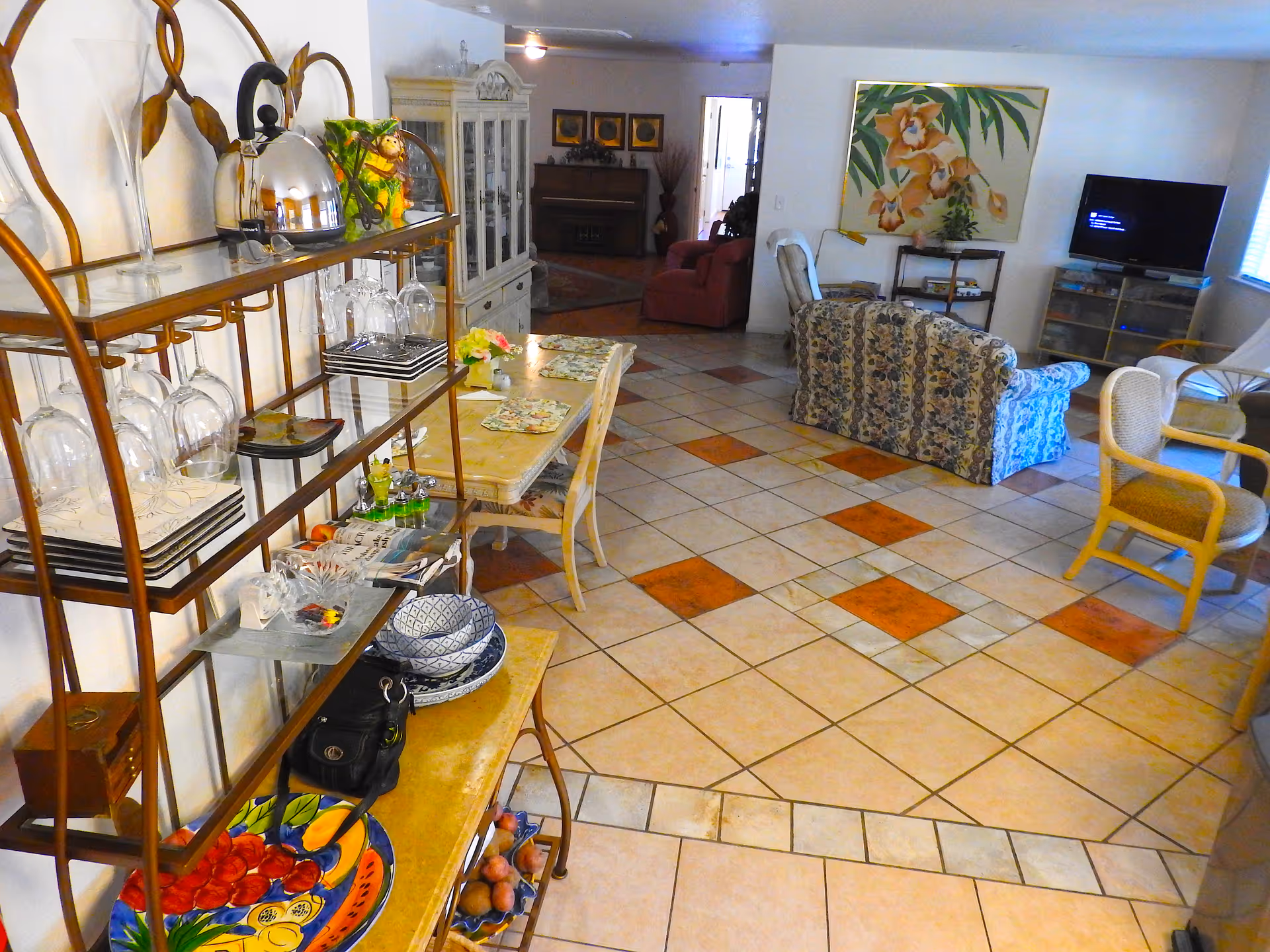 Spacious senior living lounge with couches, a dining table, glass shelves, and a TV.