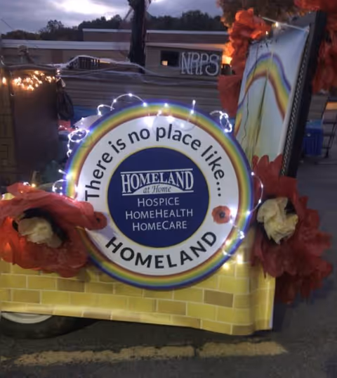Decorated parade float featuring Homeland at Home signage, rainbow lights, and red flowers.
