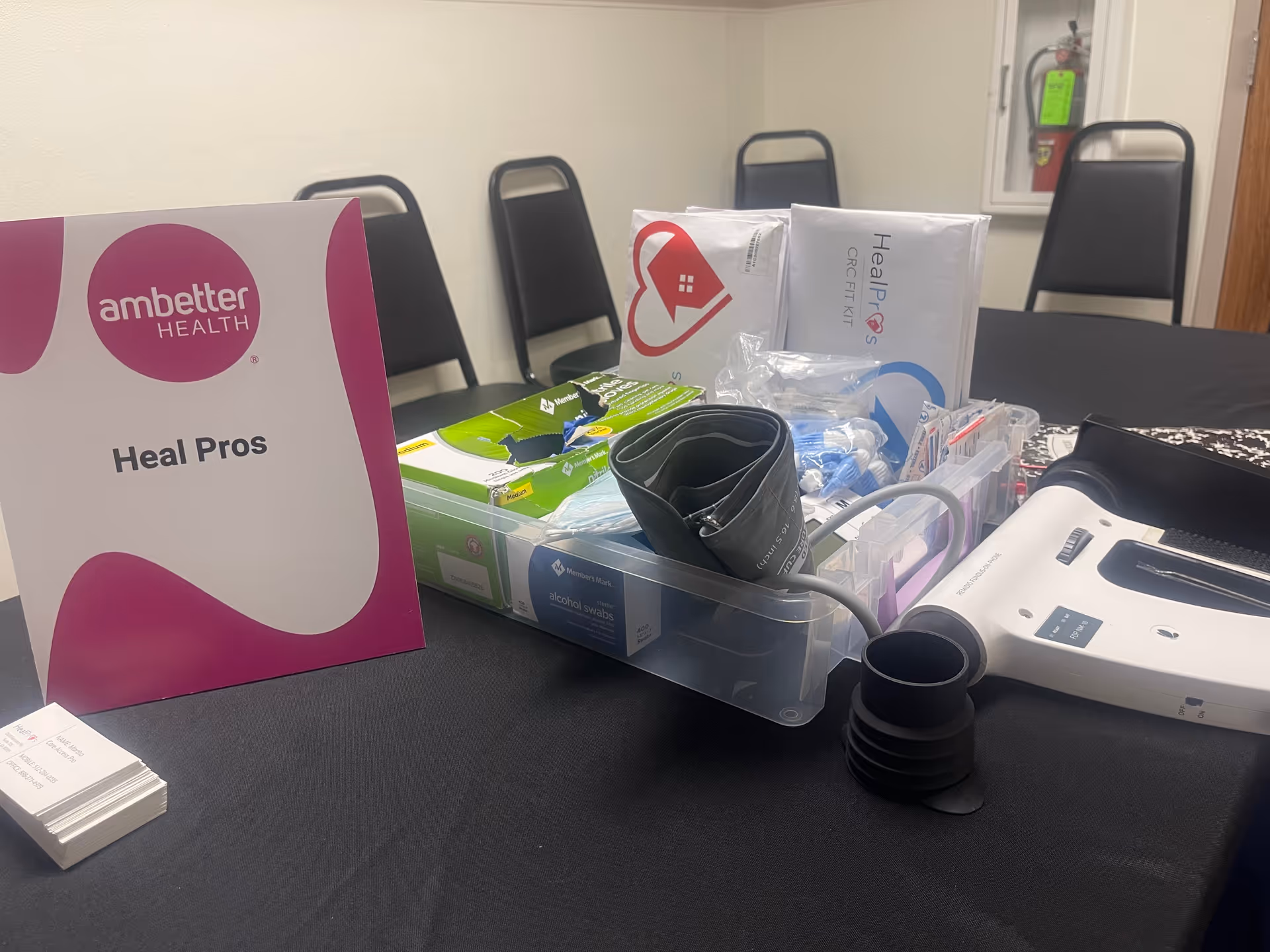 Table with medical supplies and Heal Pros materials in a room with chairs.
