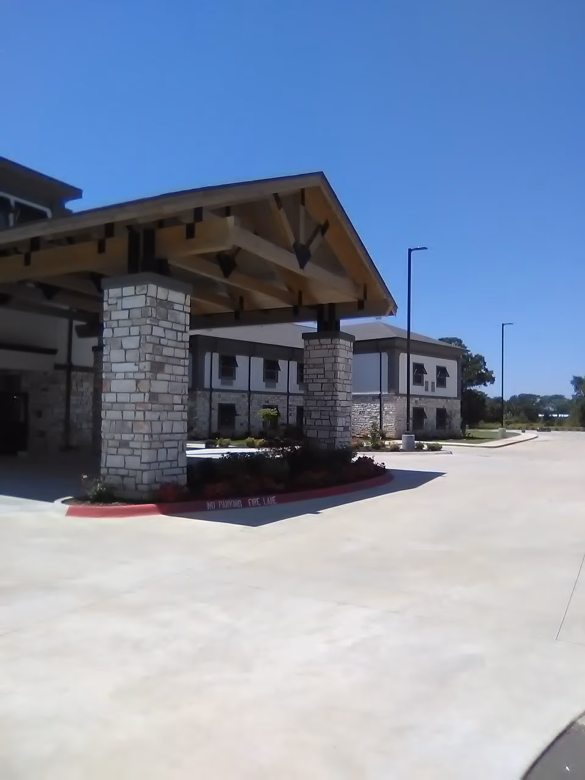 Front exterior of a facility with stone columns, a porte-cochere, and a spacious driveway.