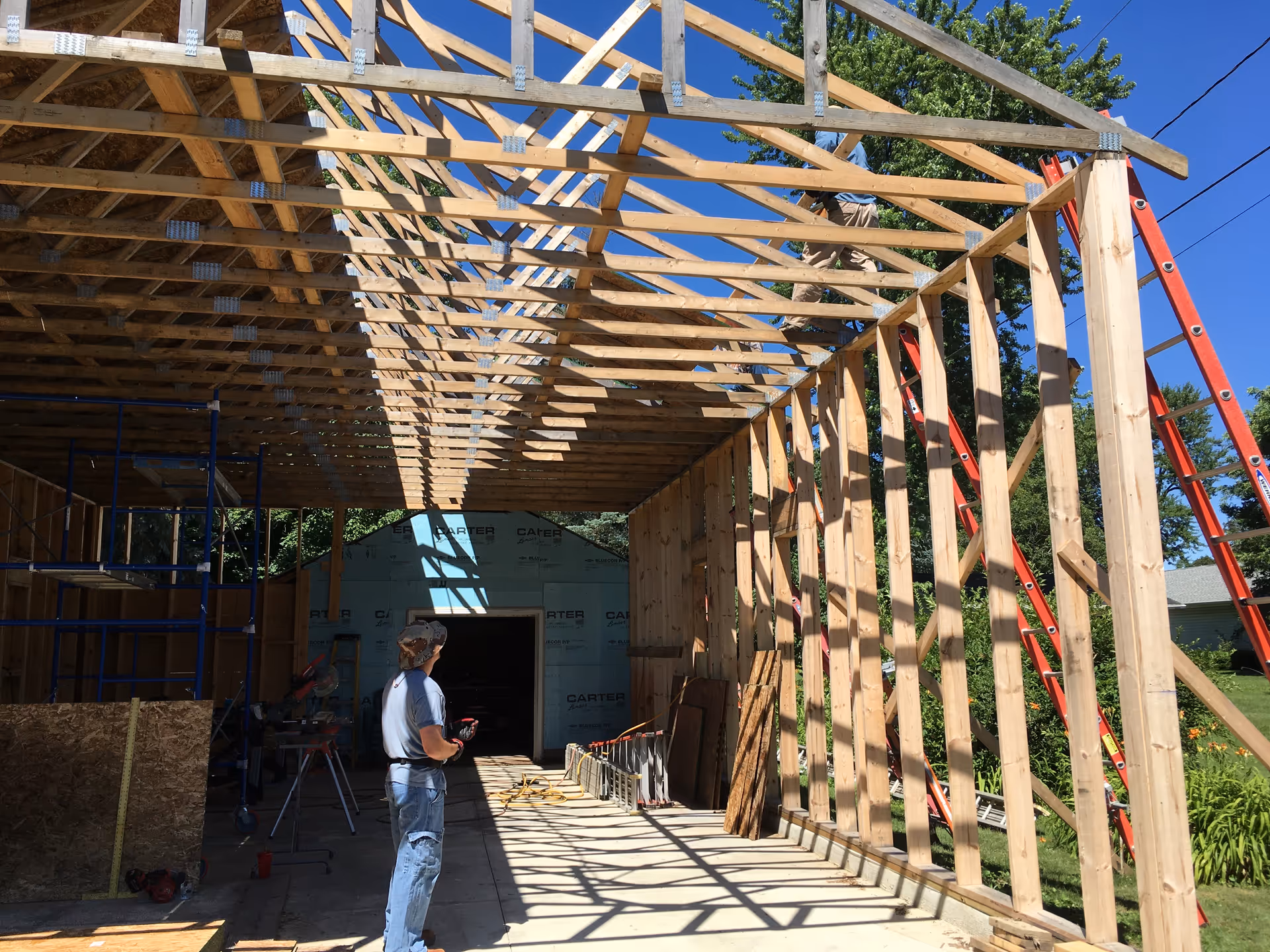 Construction site with wooden framing, scaffolding, and a worker inspecting the partially built structure.