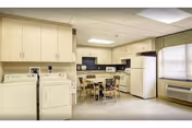Bright kitchen and dining area in a senior living facility with cabinets, appliances, and a table.