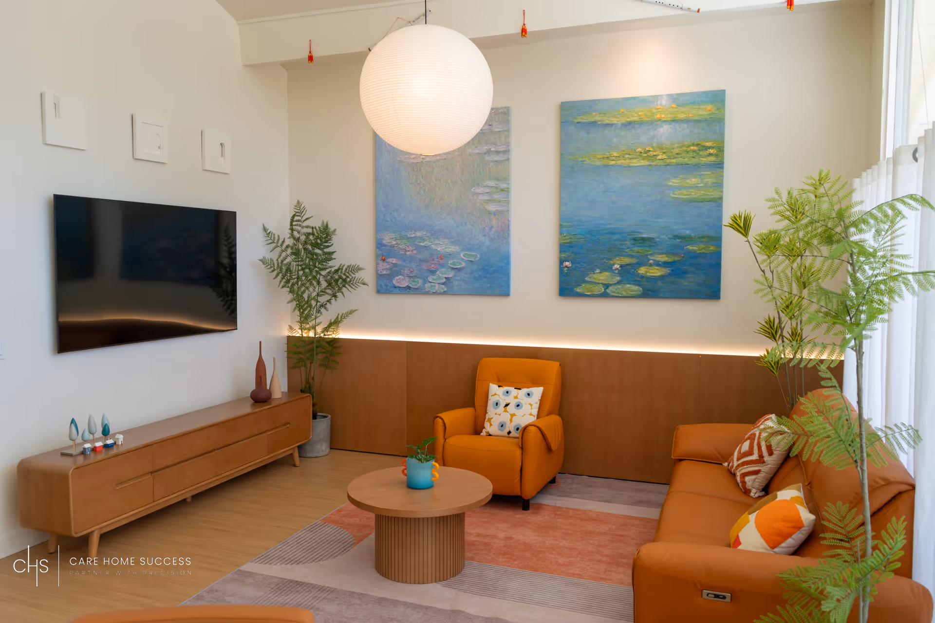 Bright living room lounge with orange seating, plants, TV, and wall art.