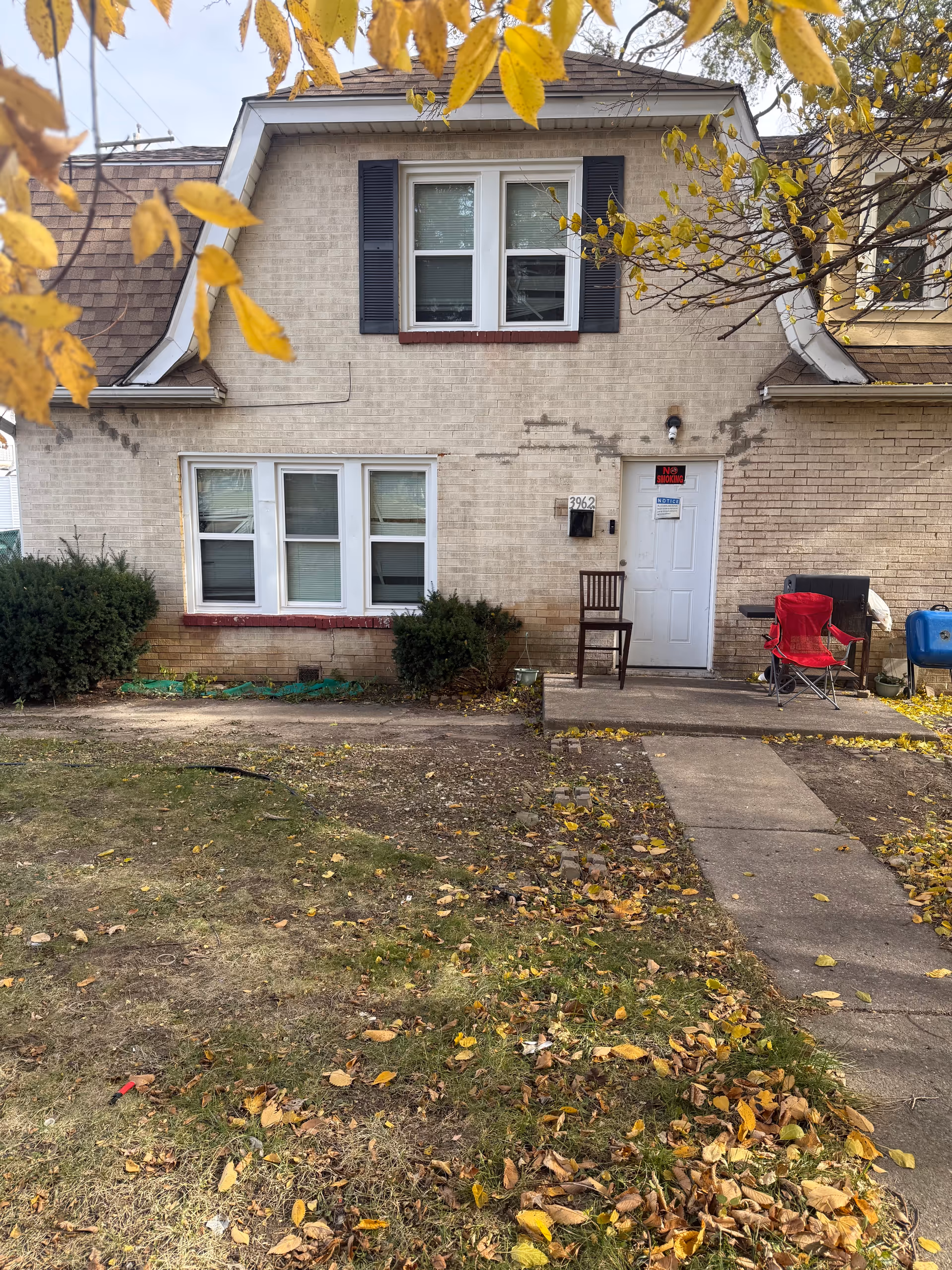 Front exterior of a brick, house-like senior care facility with chairs, path, and autumn leaves.