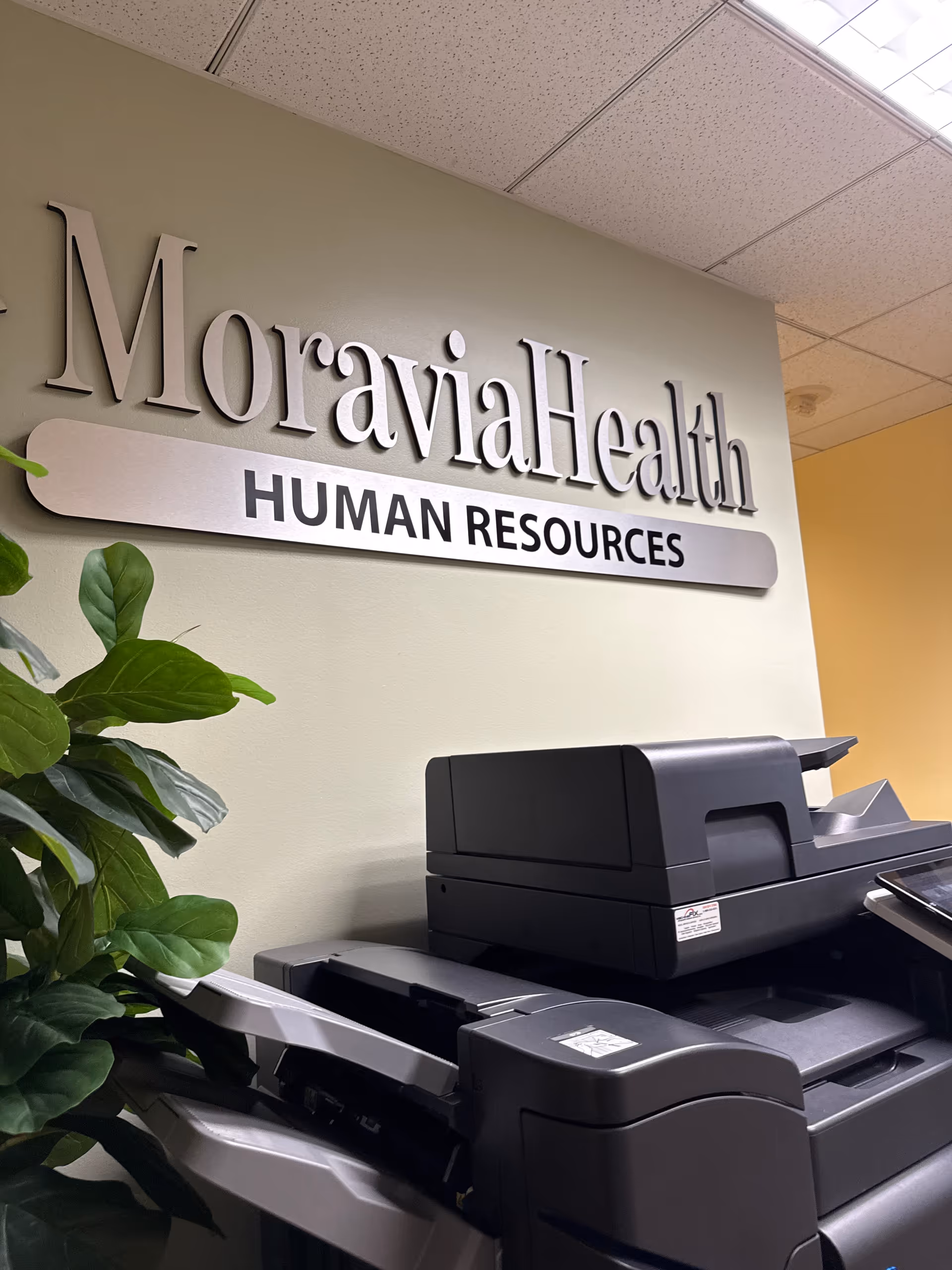 MoraviaHealth Human Resources sign on wall beside a large office printer