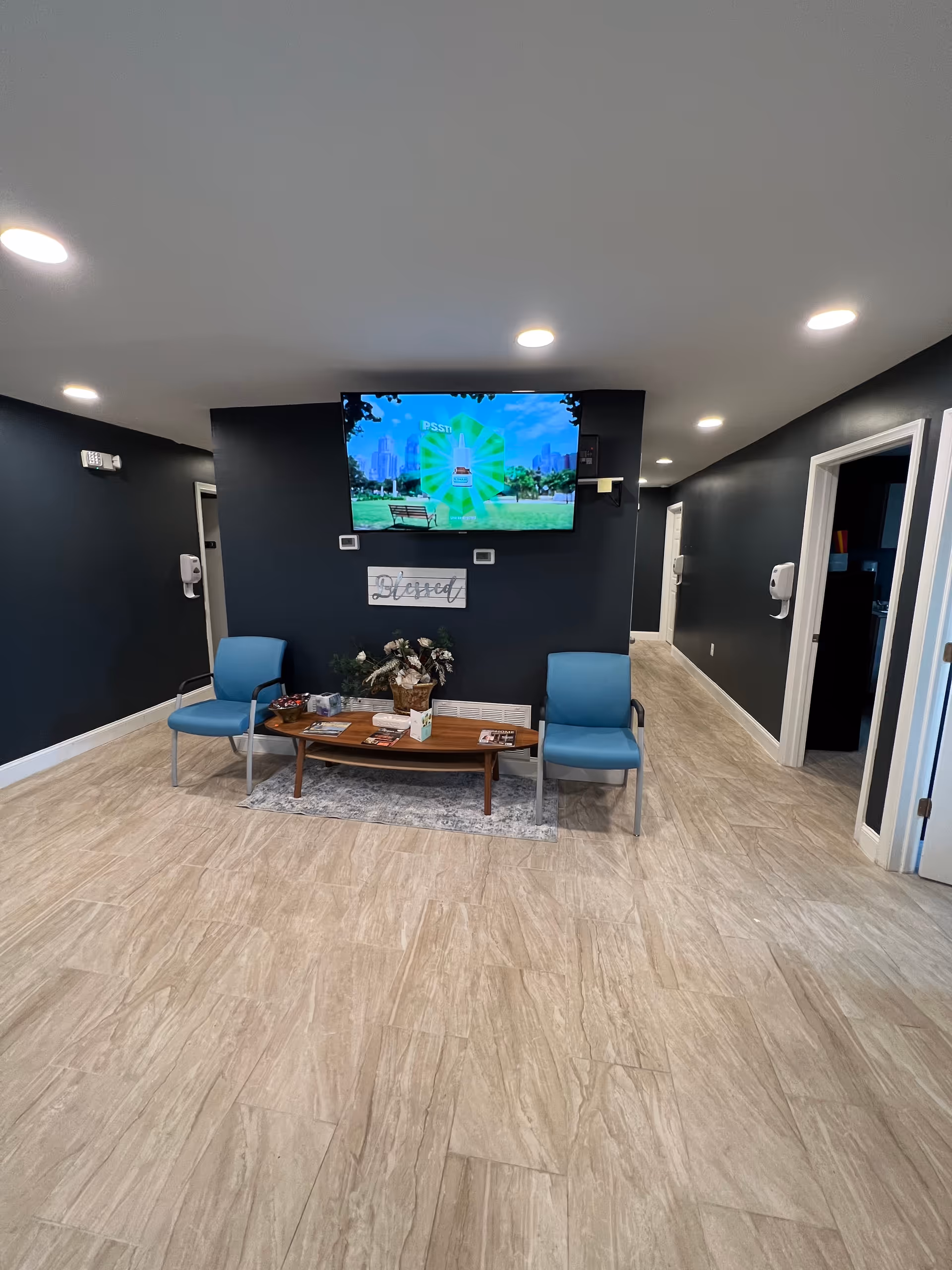 Lobby seating area with blue chairs, a coffee table, and wall-mounted TV.