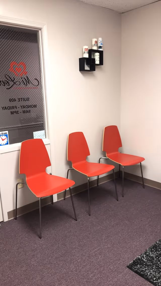 Three red chairs line a wall in a small indoor waiting area.