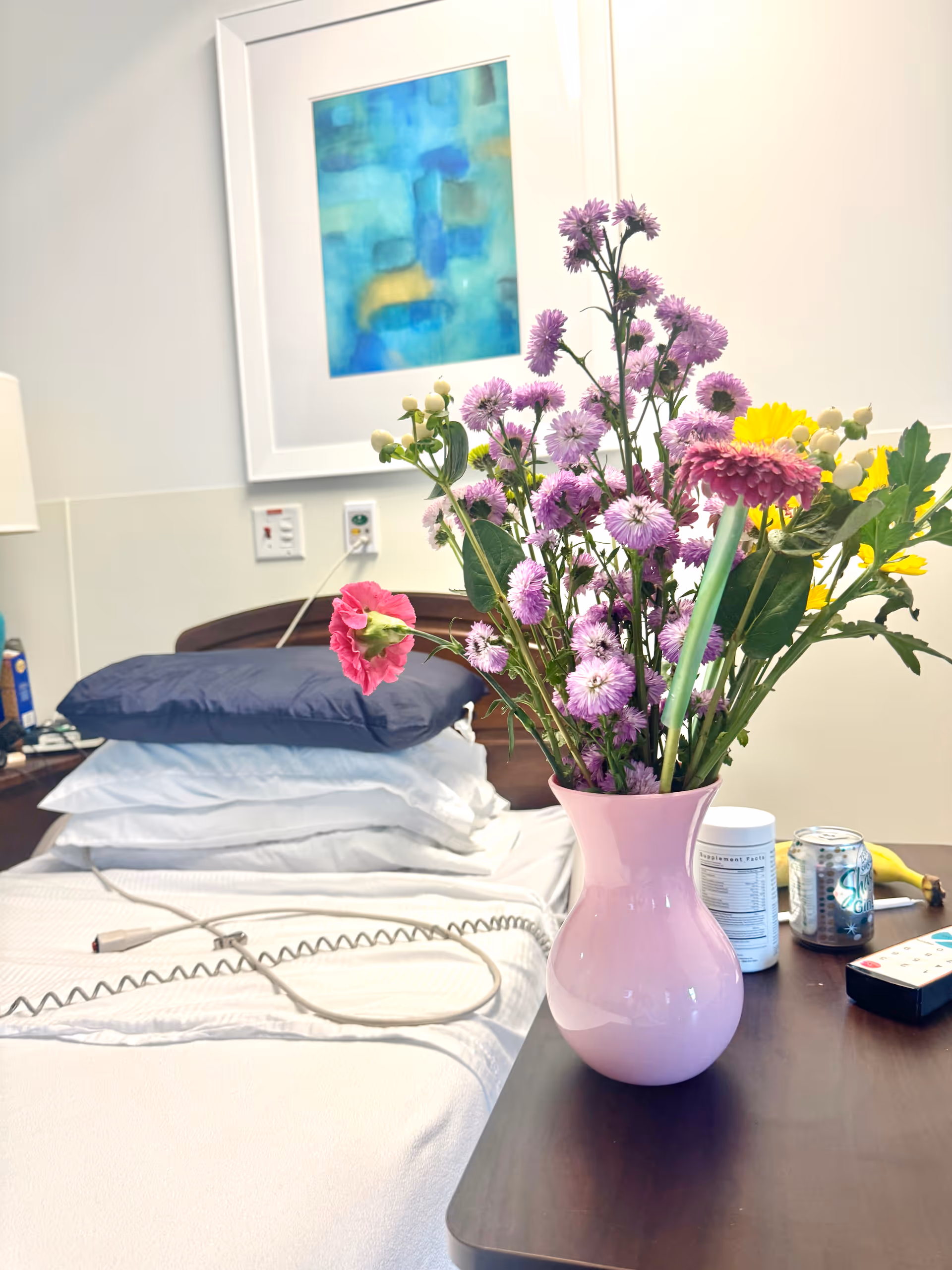 A hospital-style bed in a bedroom with a vase of colorful flowers on a bedside table.
