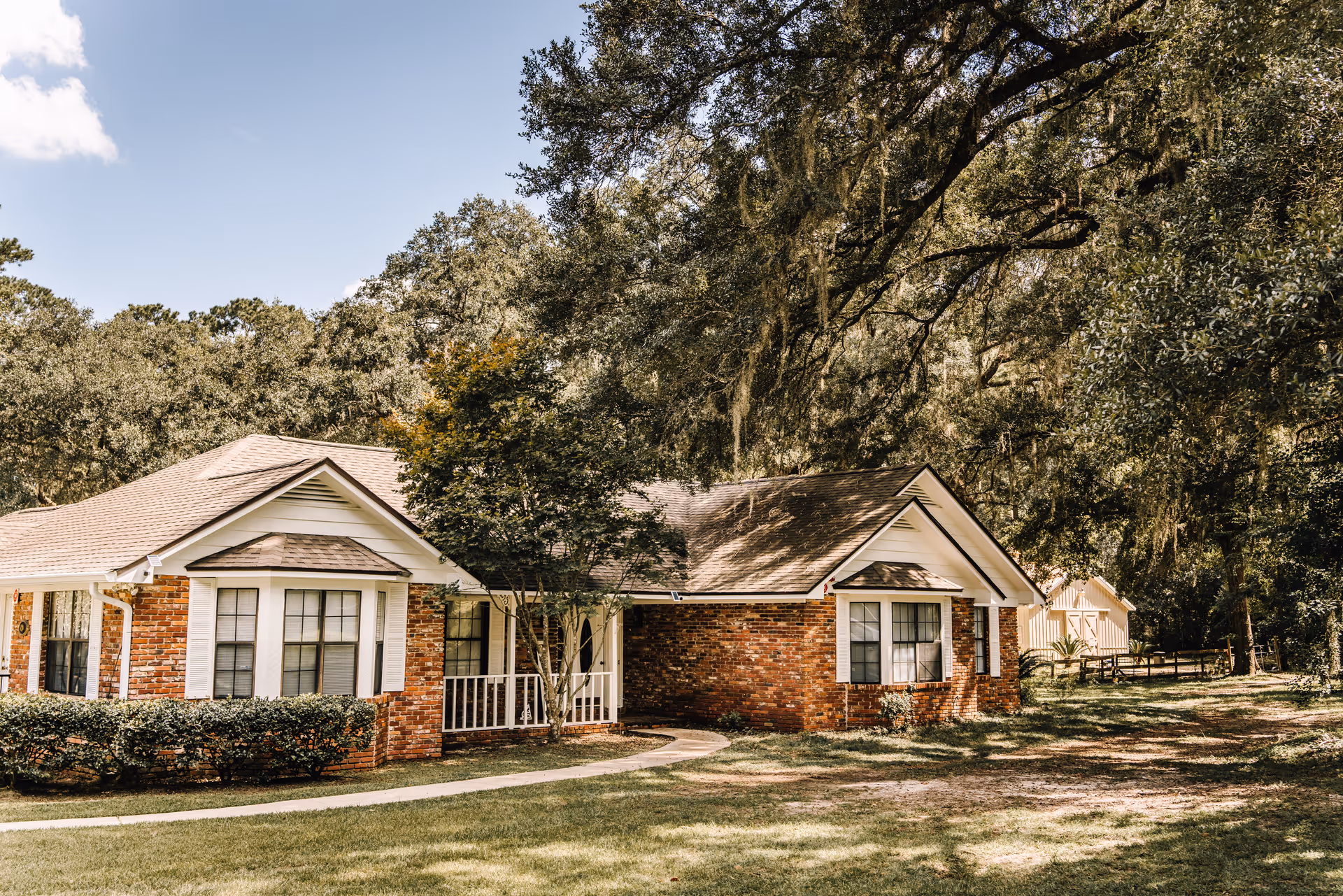 Brick single-story residence with a lawn, trees, and a curved path to the front porch.