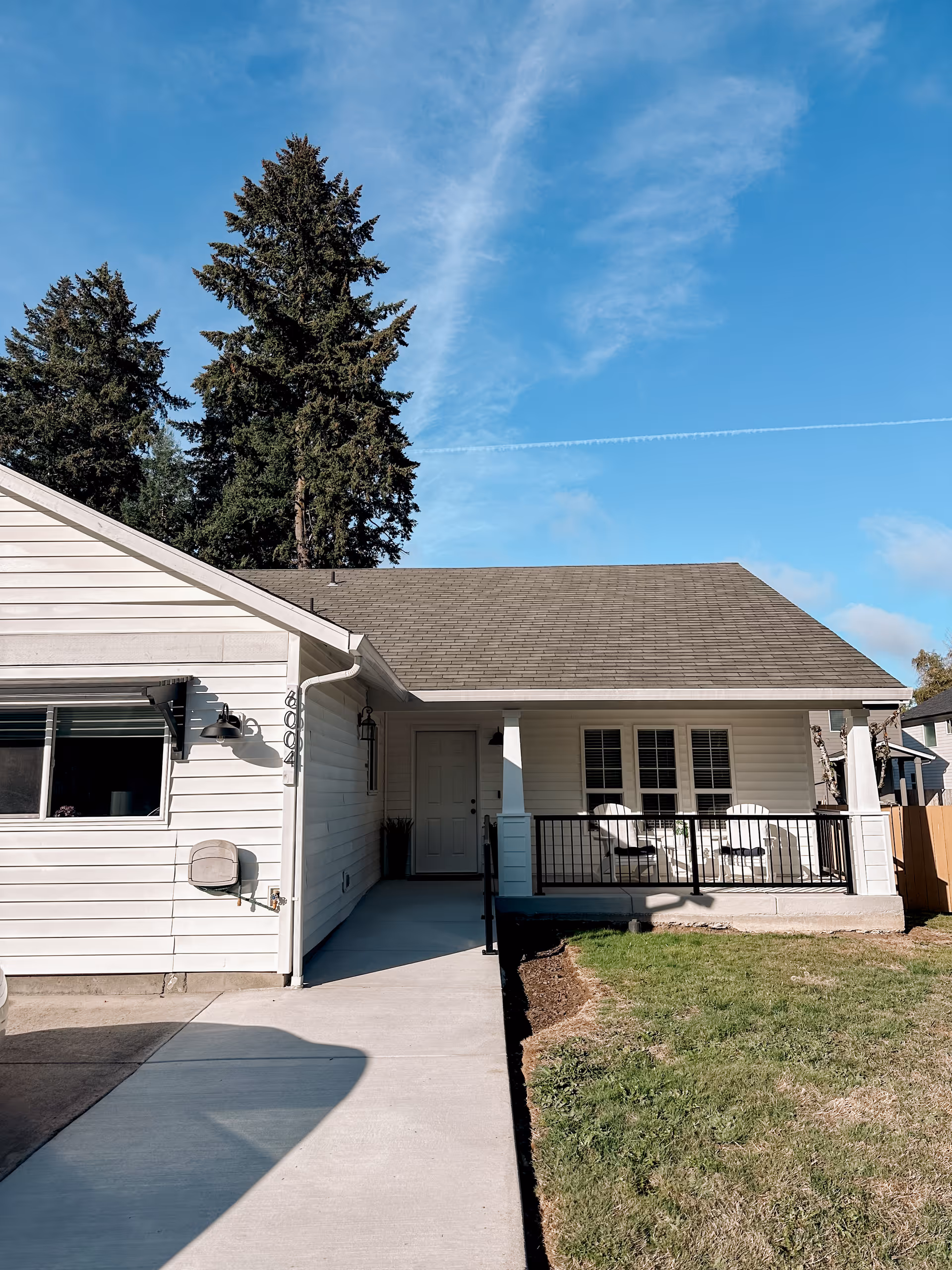 White single-story home exterior with a covered porch and outdoor seating.
