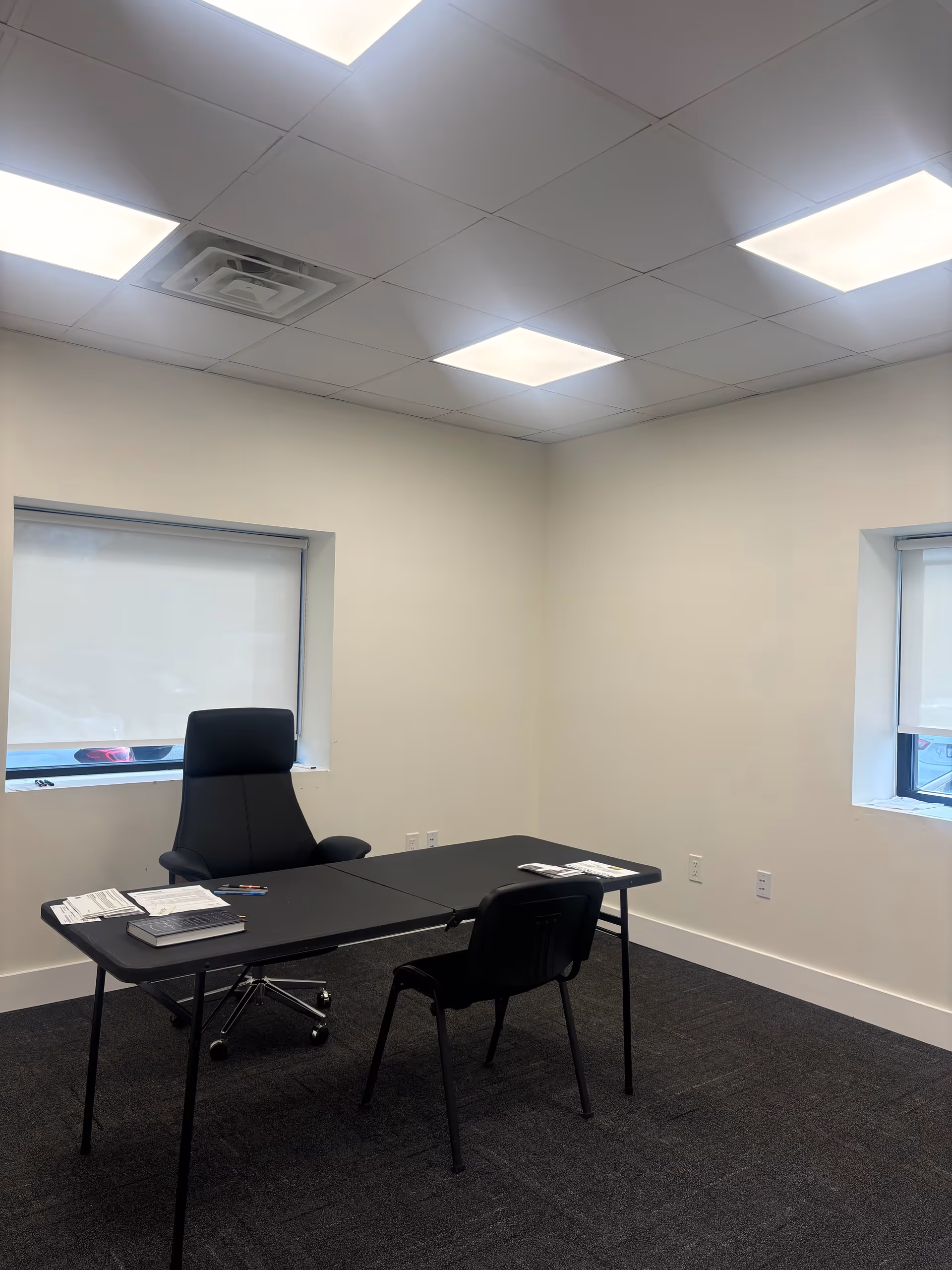 A minimal office with a black desk, executive chair, and two windows.
