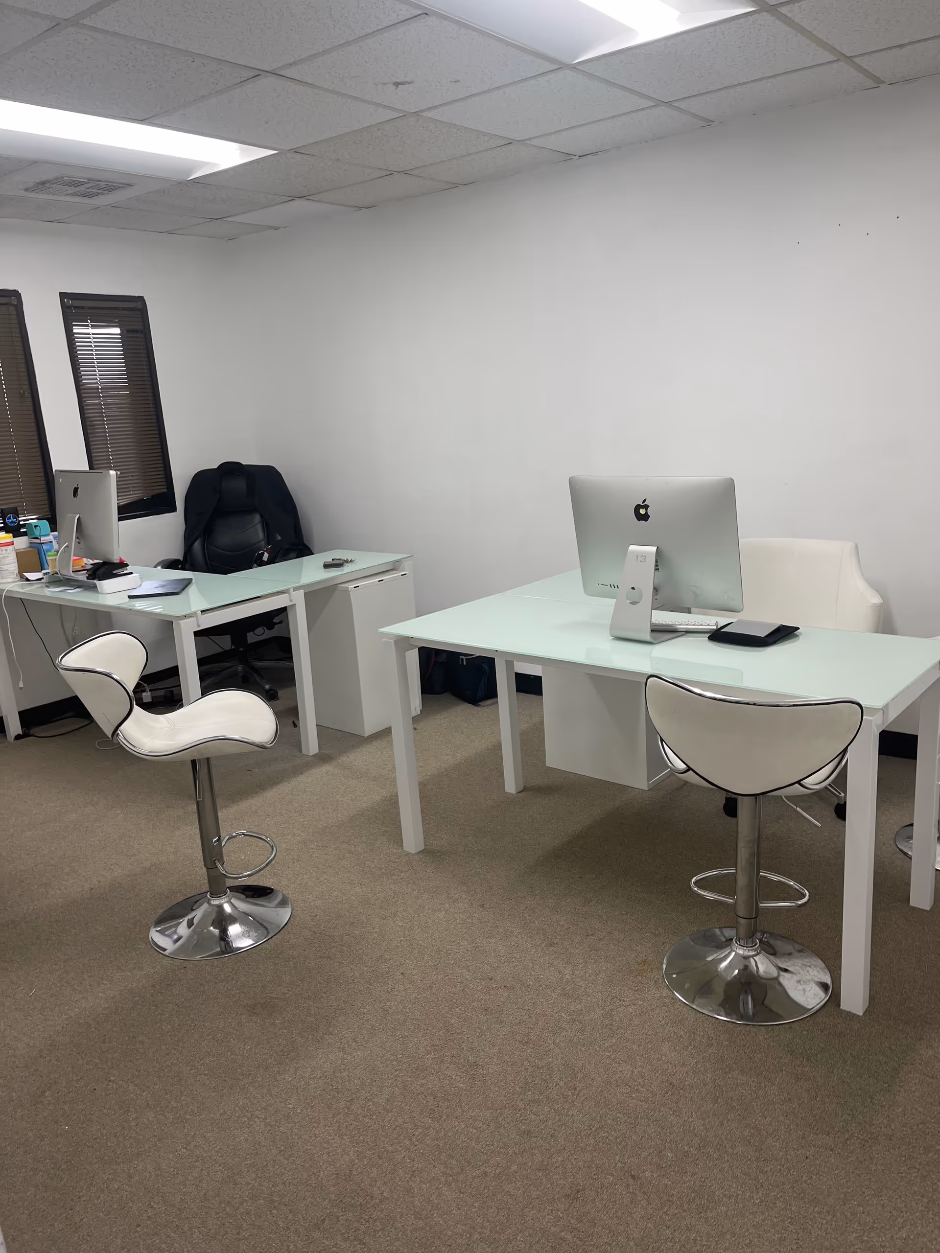 Bright office area with glass desks, white chairs, and two computer workstations.