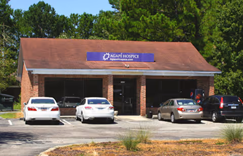 Exterior view of Agapé Hospice building with several cars parked in front.