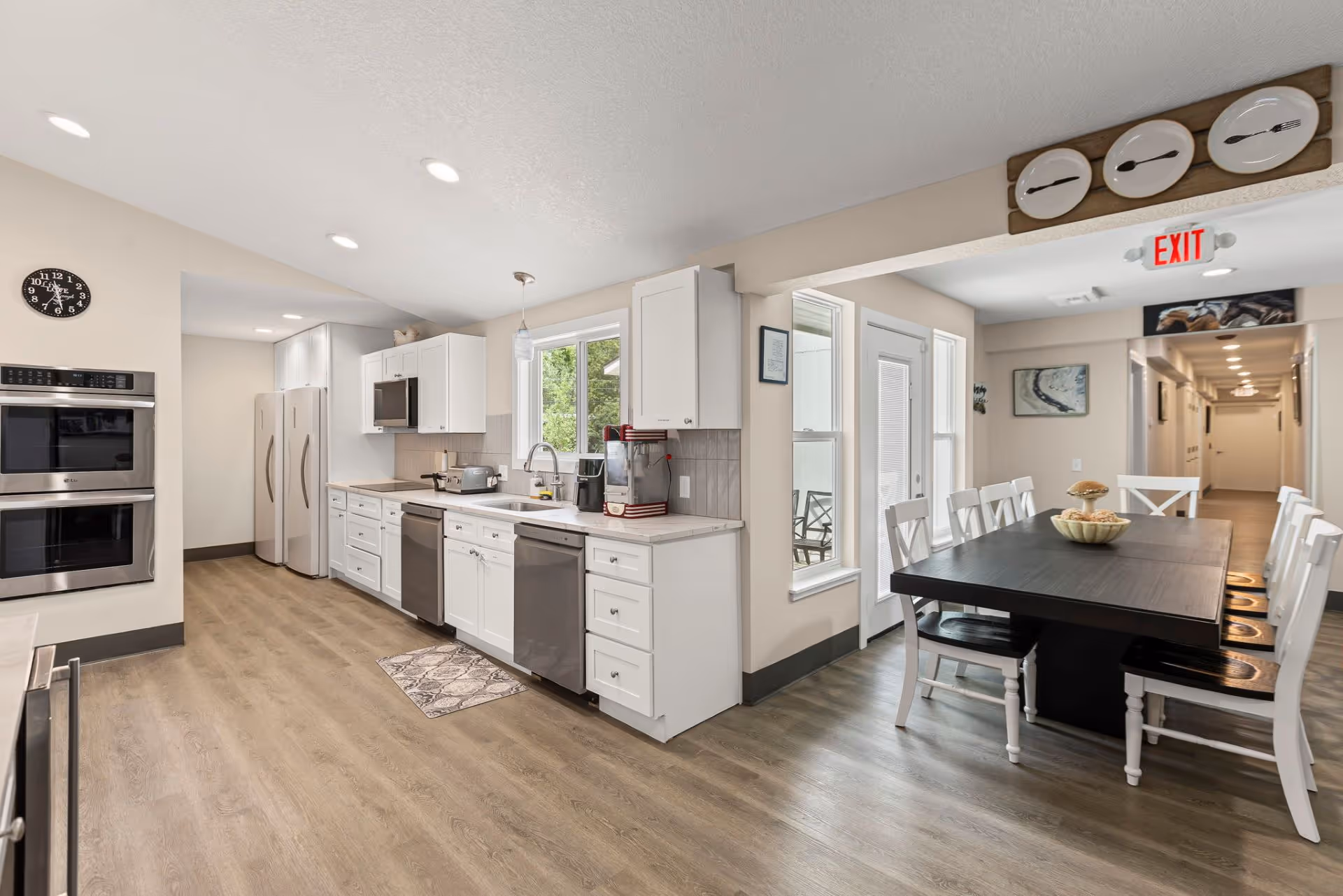 Bright open kitchen and dining area with white cabinets and dark dining table.