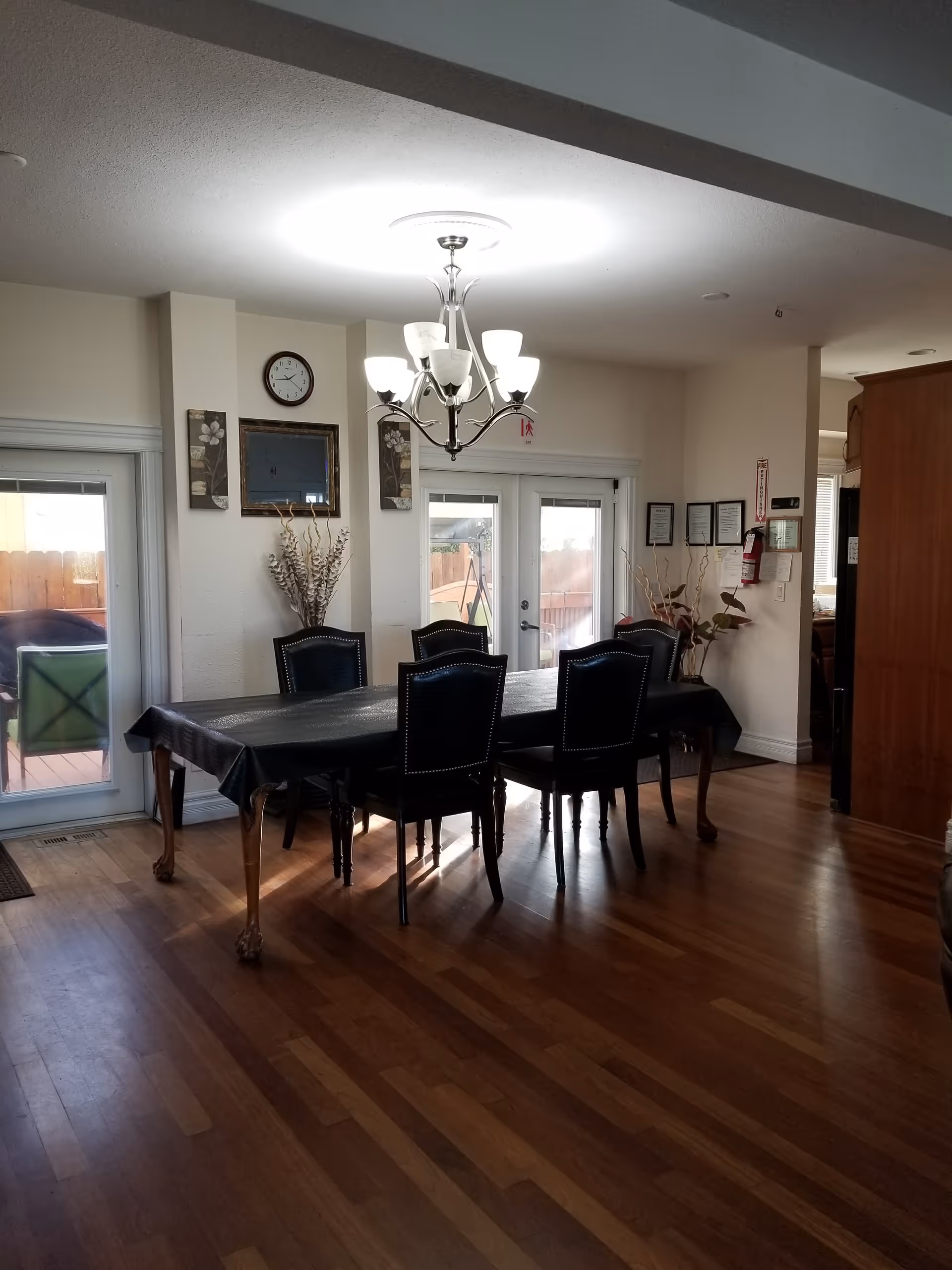 Dining room with a long table, dark upholstered chairs, chandelier, and wooden floors.