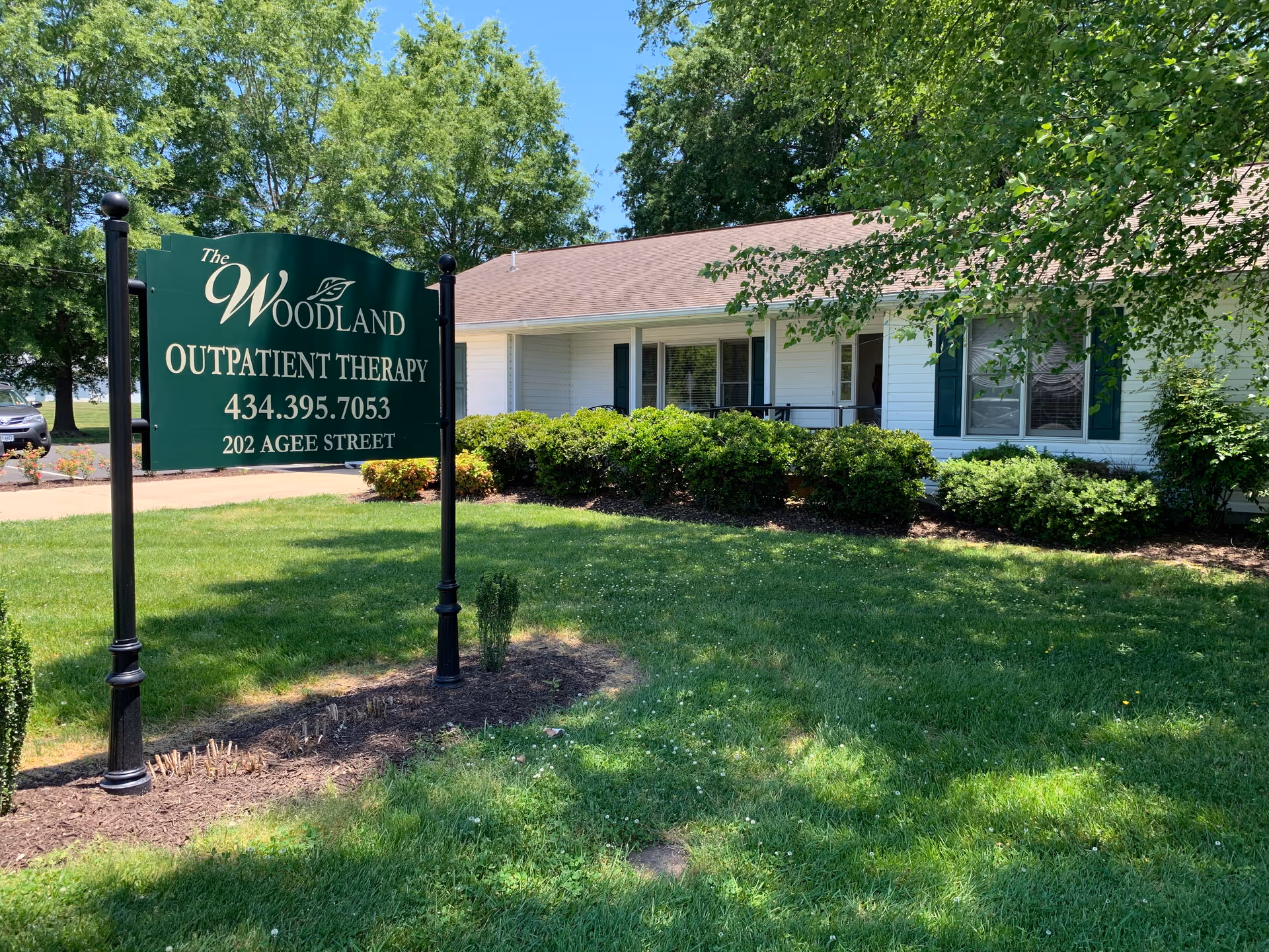 Exterior view of The Woodland building with a green outpatient therapy sign and manicured lawn.