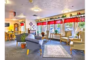 Bright communal living room in a senior care center with seating and windows.