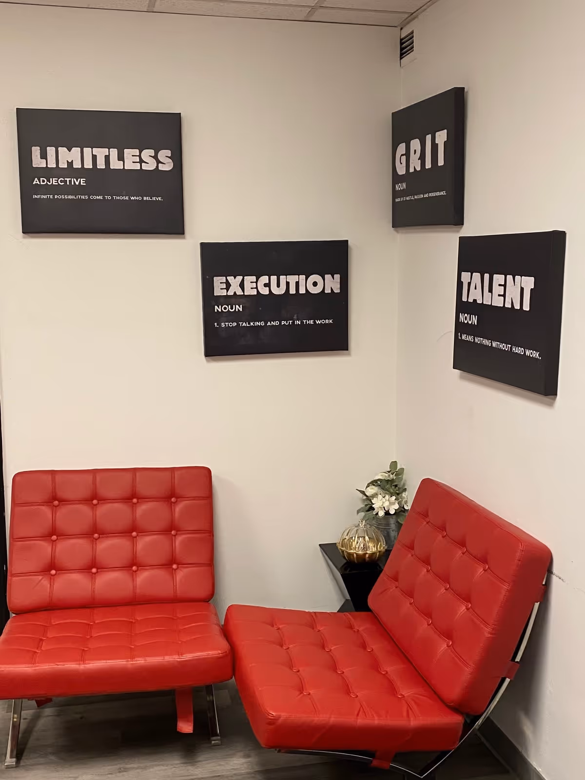 Two red tufted lounge chairs flank a small side table beneath motivational wall art.