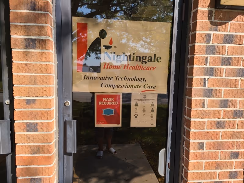 Brick building entrance with Nightingale Home Healthcare sign on glass door and posted notices.