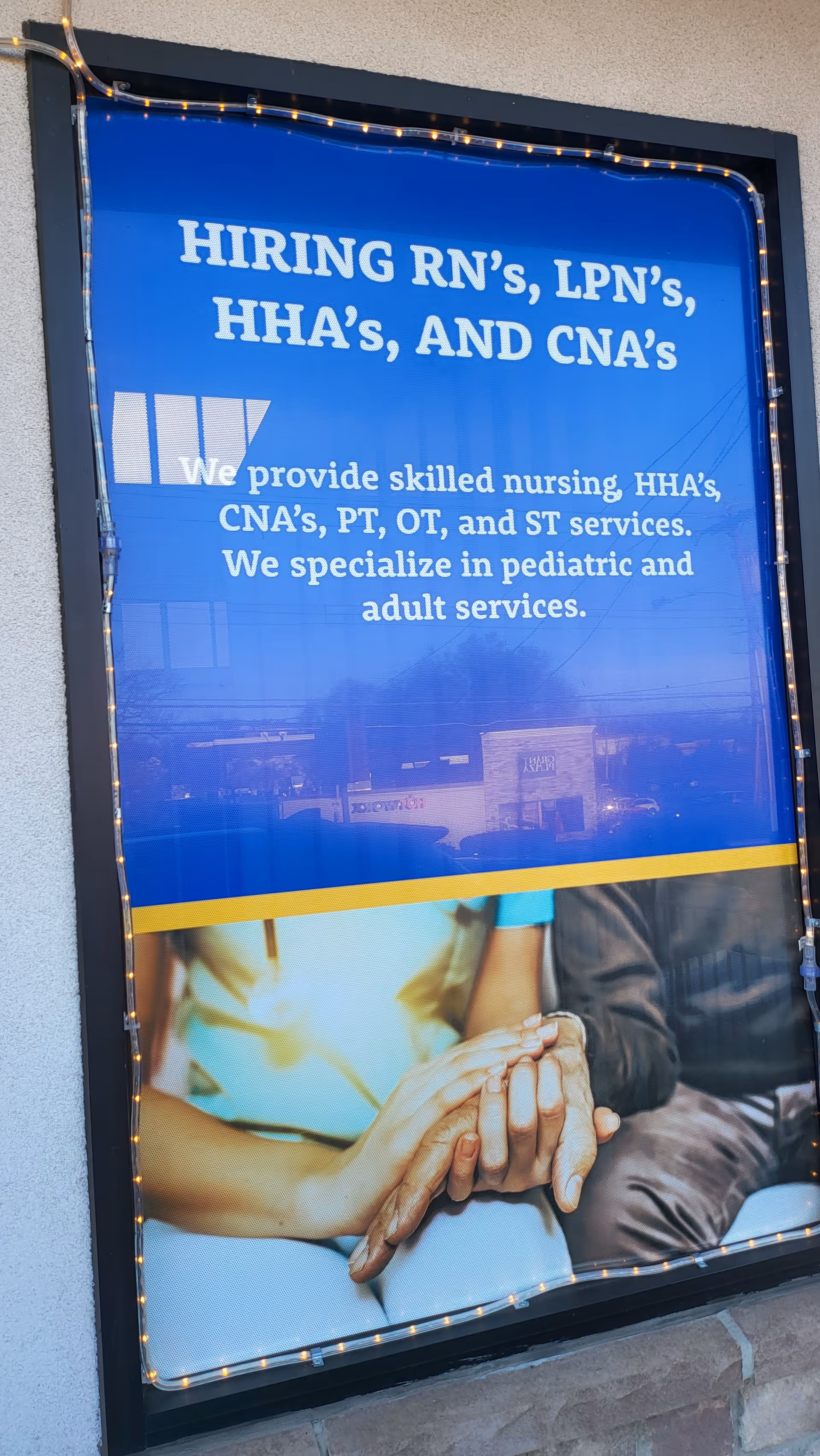 Blue storefront window sign advertising RN/LPN/CNA hiring at Amazing Care Home Health Services.