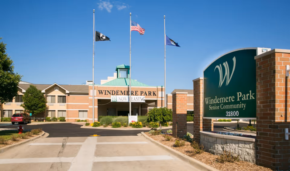 Entrance and front sign of the Windemere Park senior community with flags flying and the building behind.