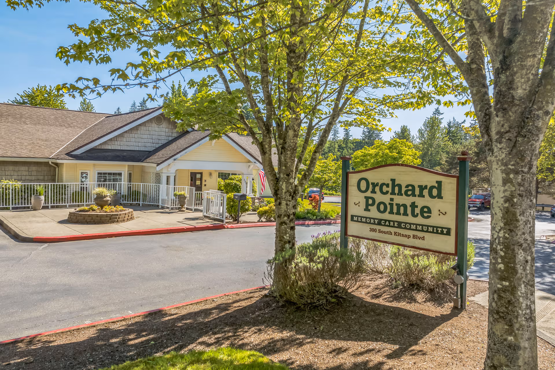 Exterior view of Orchard Pointe by Cogir showing entrance, sign, trees, and landscaped walkway.