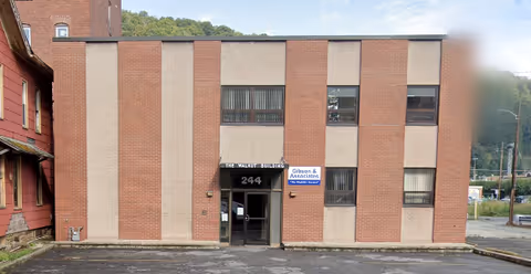Brick two-story building with a central glass entrance and surrounding asphalt parking area.