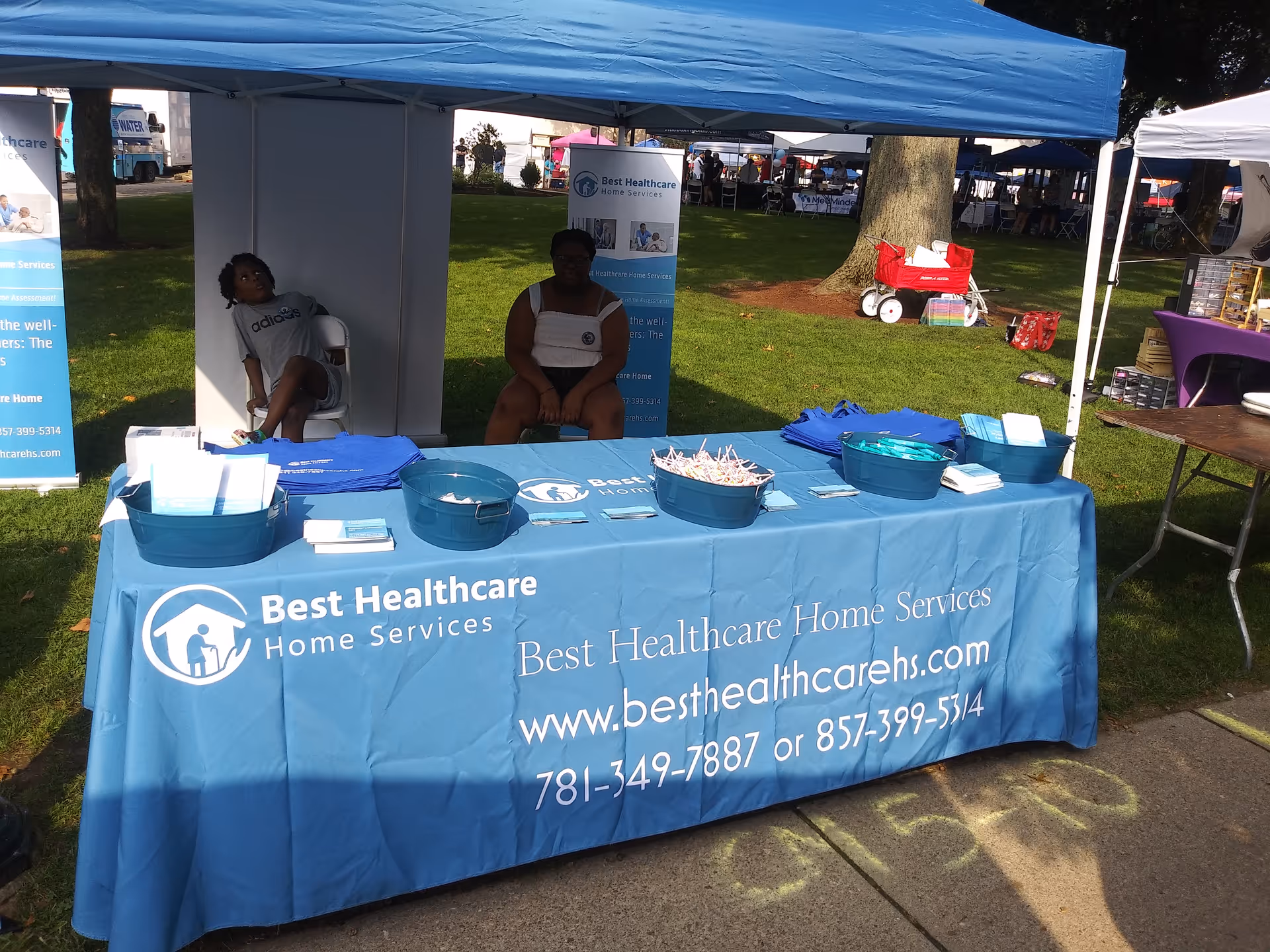 Outdoor promotional booth for Best Healthcare Home Services with a blue tablecloth and staff.