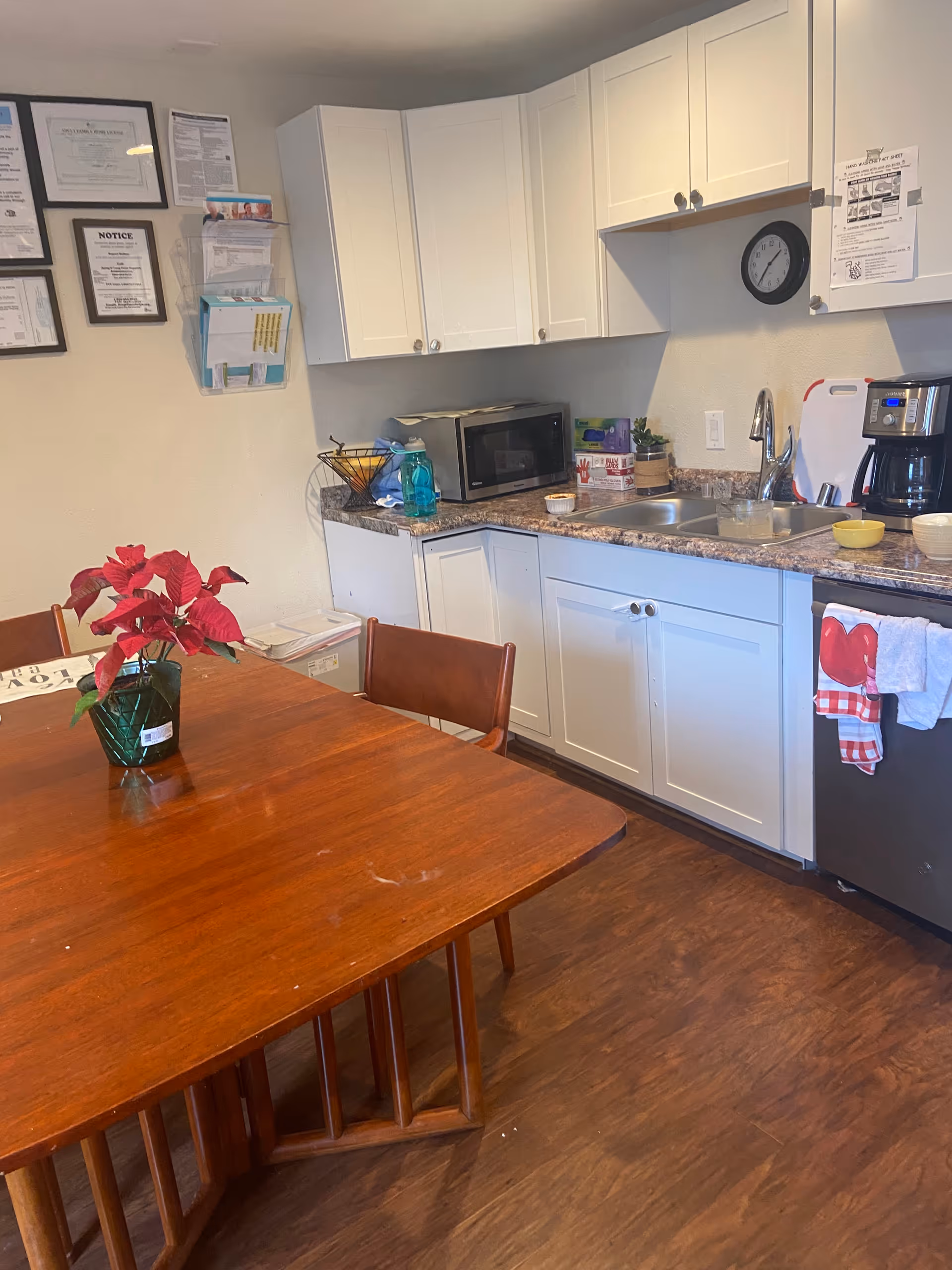 Bright kitchenette with white cabinets, granite counters, microwave, sink, and wooden dining table.