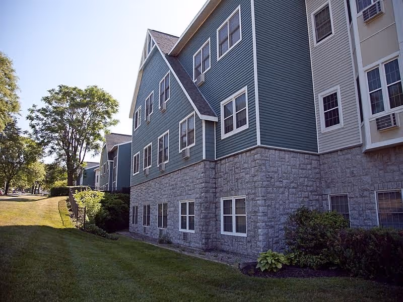 Exterior view of a blue-siding, multi-story senior living building with a stone base.