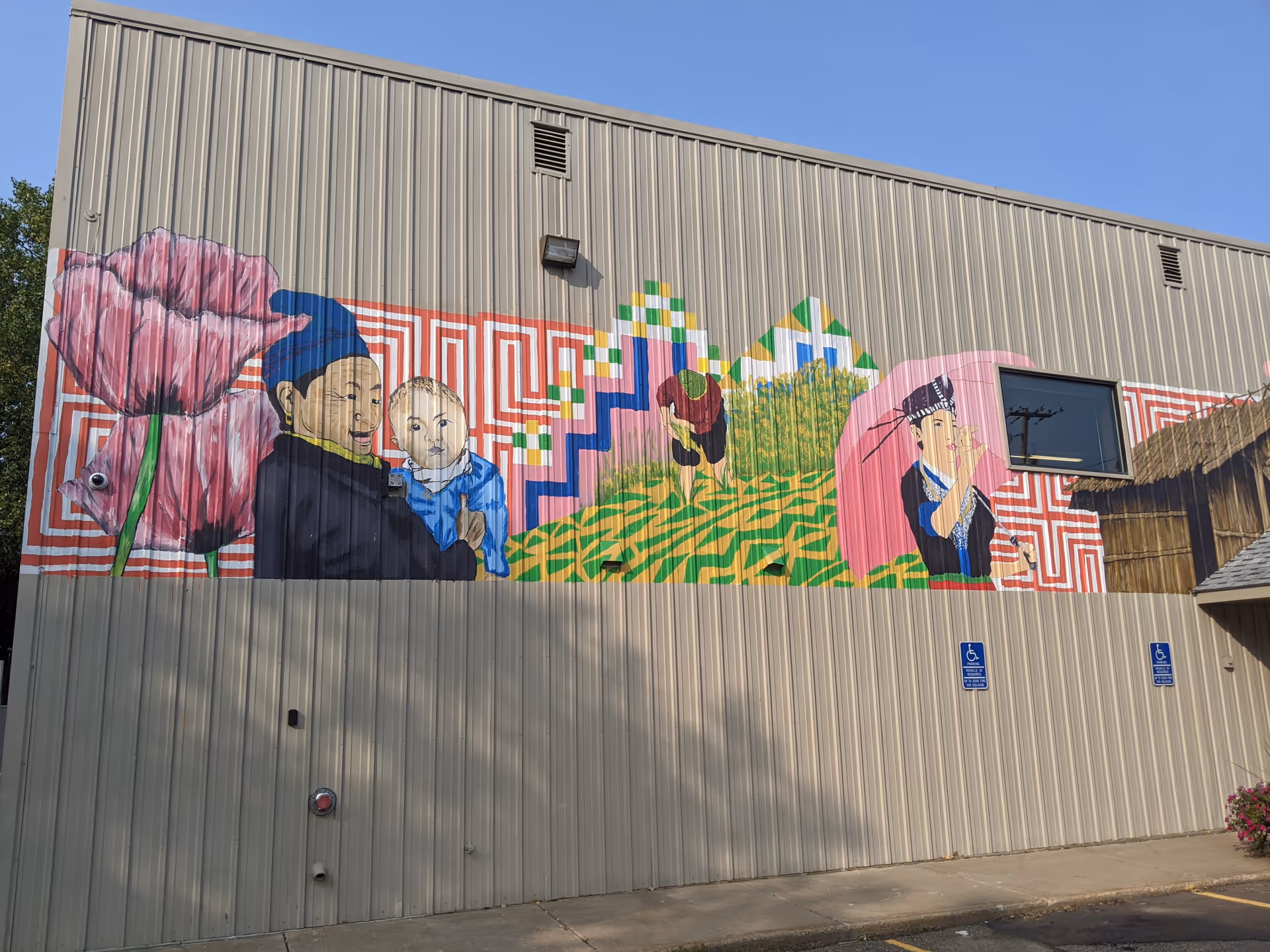 Exterior metal-walled building with a colorful mural depicting people and geometric patterns.