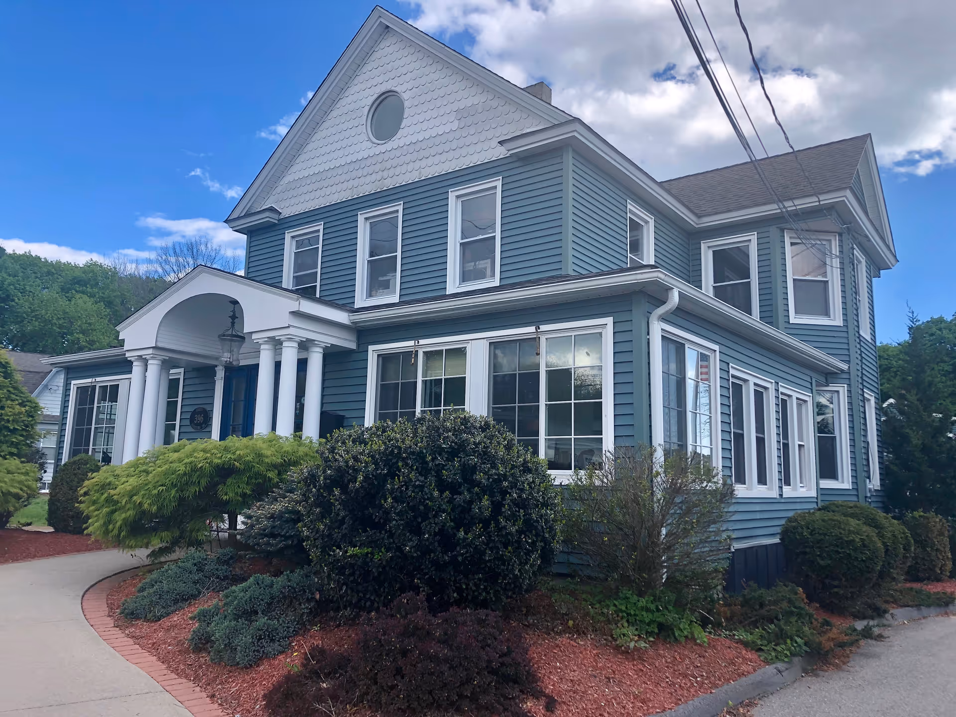 Blue two-story senior living facility exterior featuring a front porch and landscaped yard.