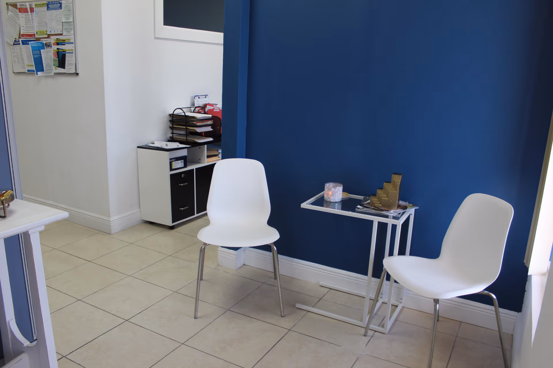 Reception area with white chairs, blue wall, and tiled floor.
