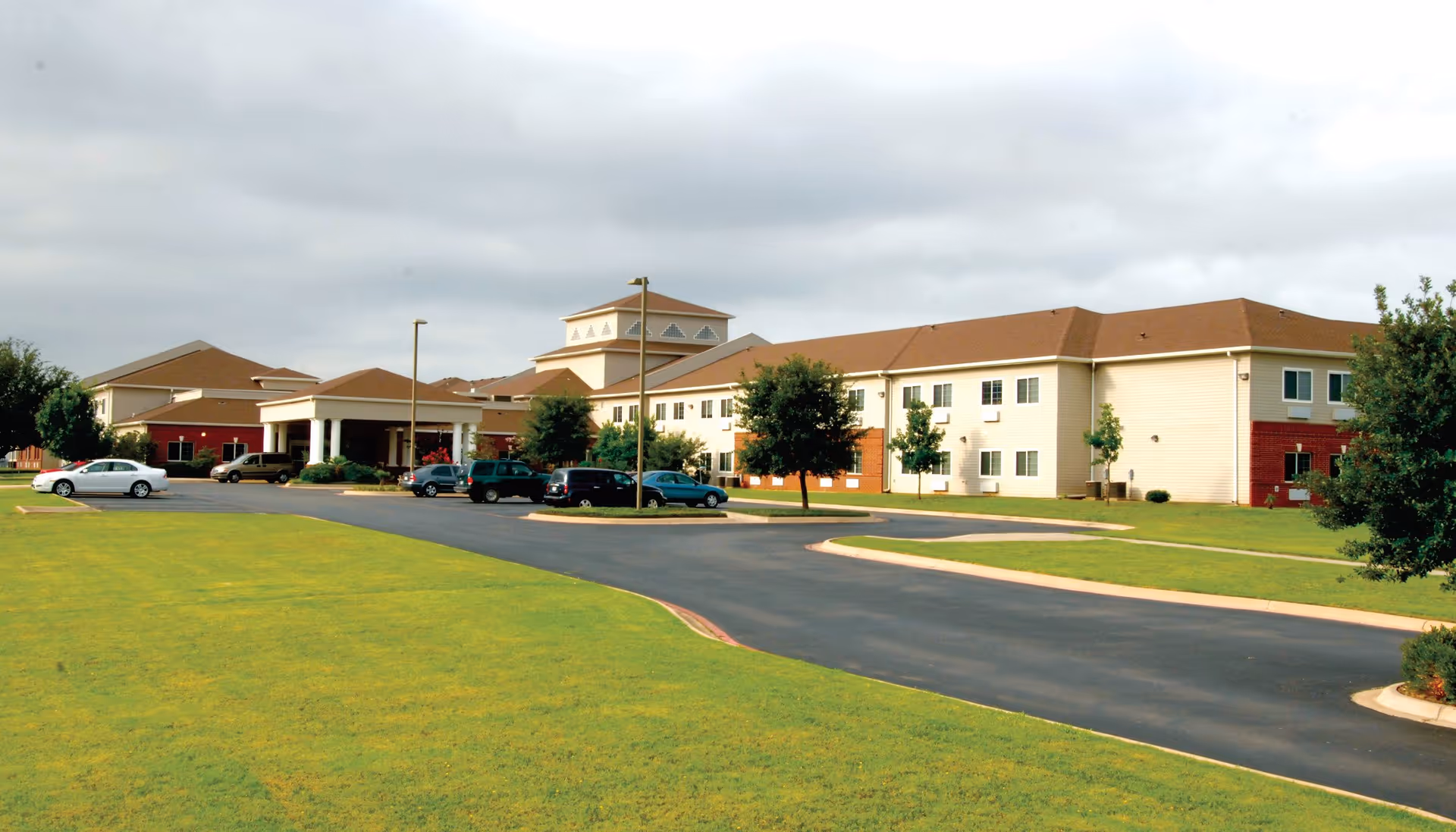 Lyndale San Angelo Senior Living facility exterior with curved driveway, parking, and green lawn.