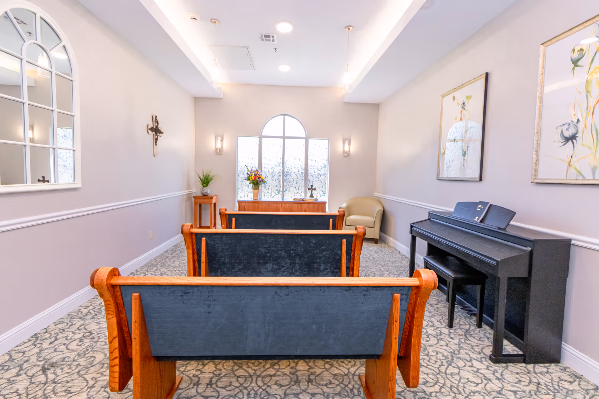 Chapel-style lobby at Magnolia Manor with pew benches, piano, arched window, and floral artwork.