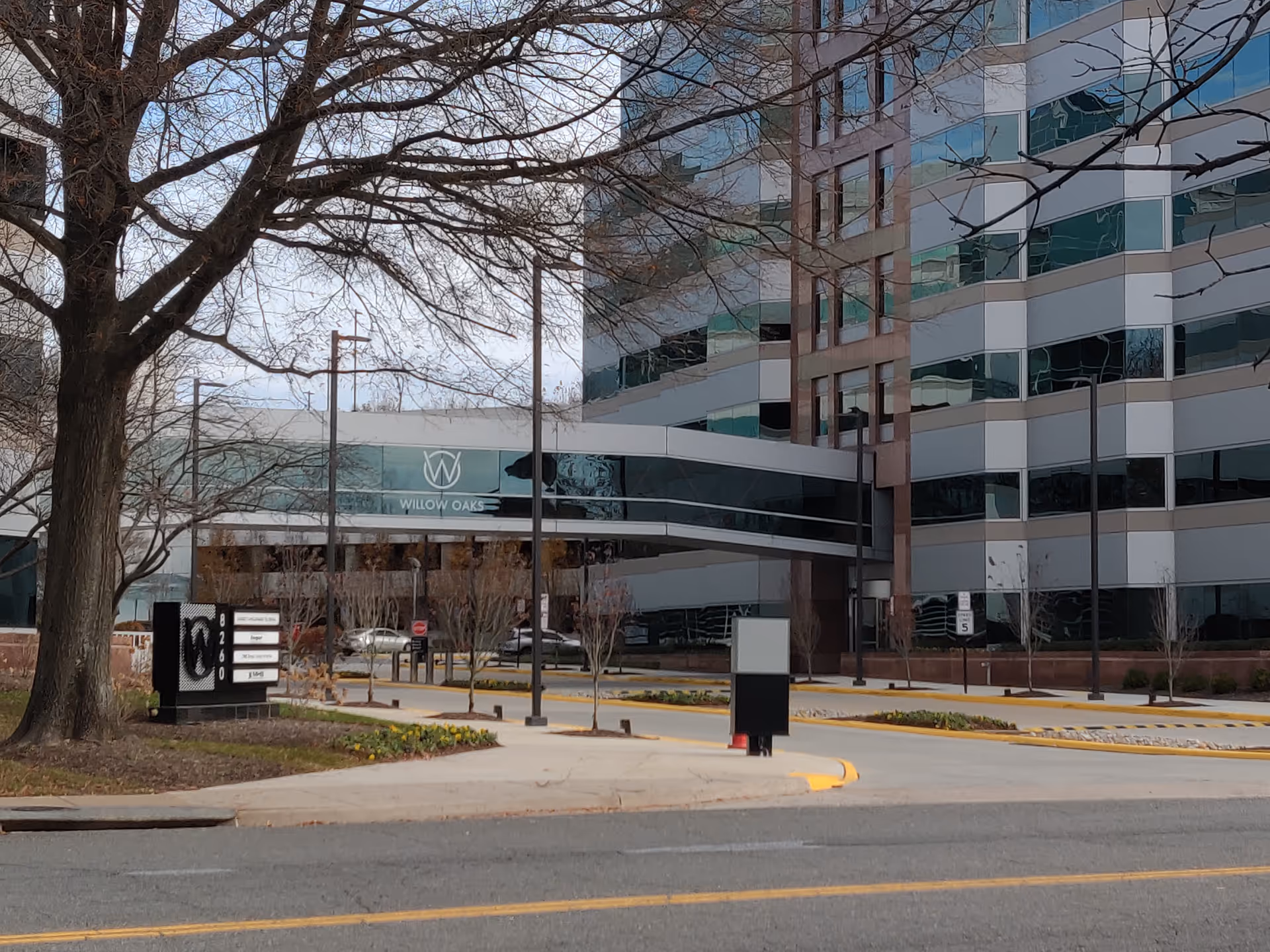 Exterior view of a modern building with a skybridge and Willow Oaks sign.