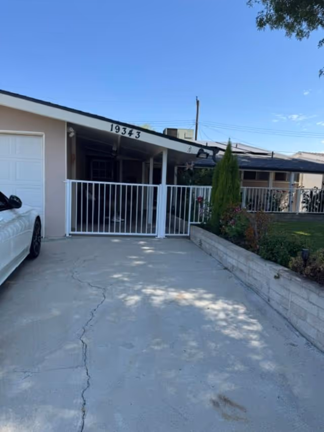 Driveway leads to a single-story senior facility with a white front gate and porch.
