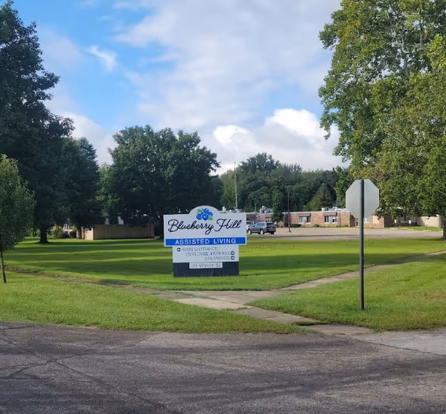 Blueberry Hill Assisted Living sign on a grassy lawn near the building entrance.