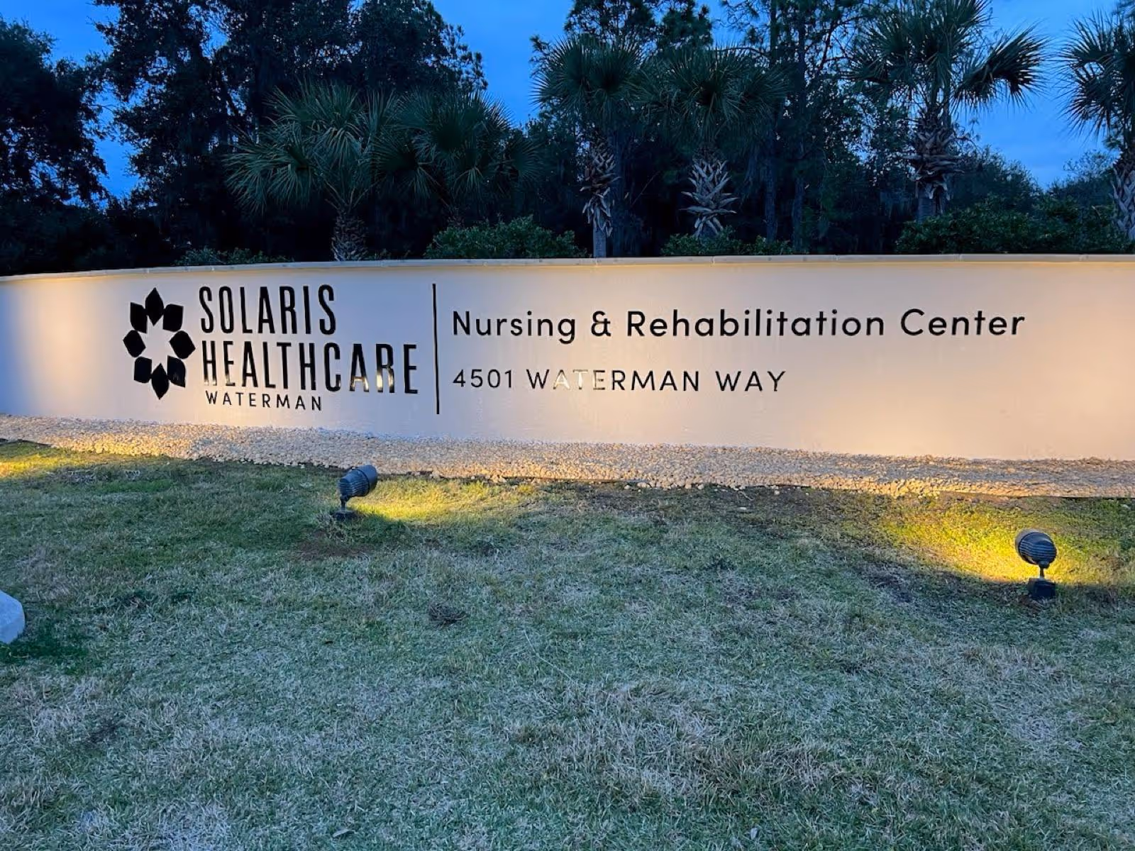 Exterior view of Solaris Healthcare Waterman sign with landscaping and palm trees at dusk.