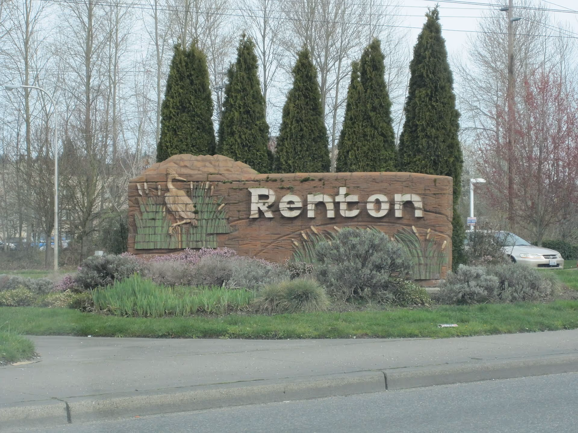 Large stone Renton sign with landscaped bushes and tall trees in front.