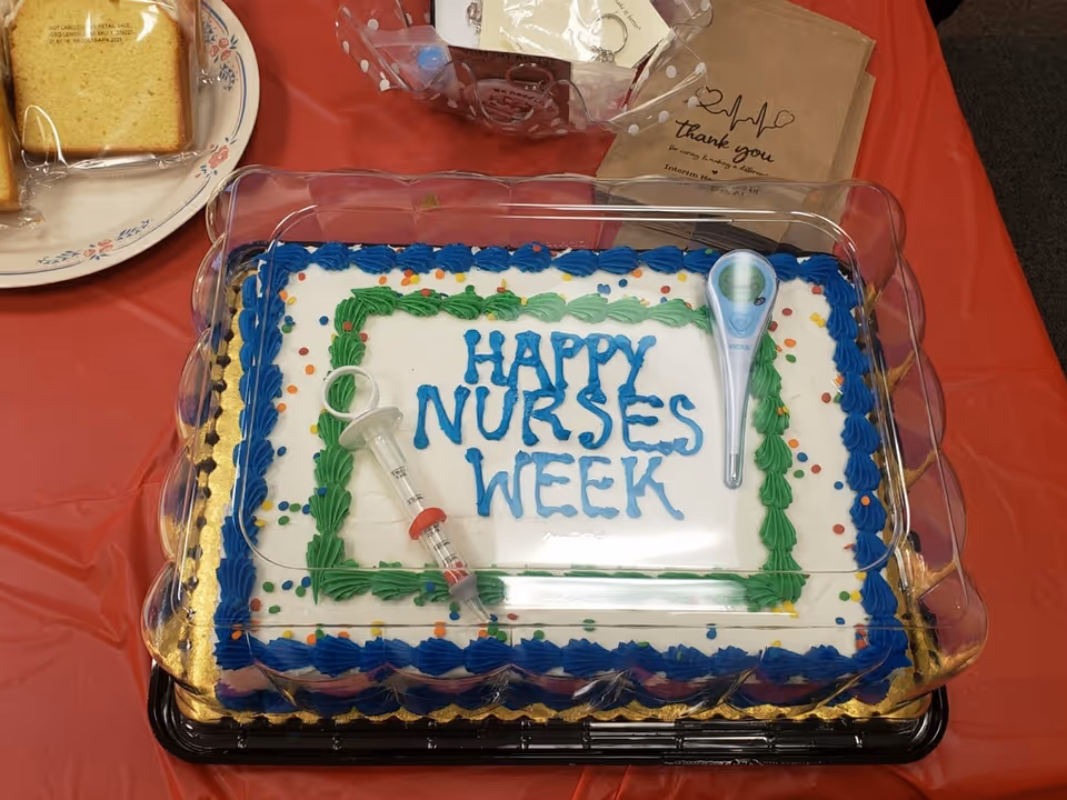 Cake on a table celebrating Nurses Week with syringe toppers and blue-green frosting.
