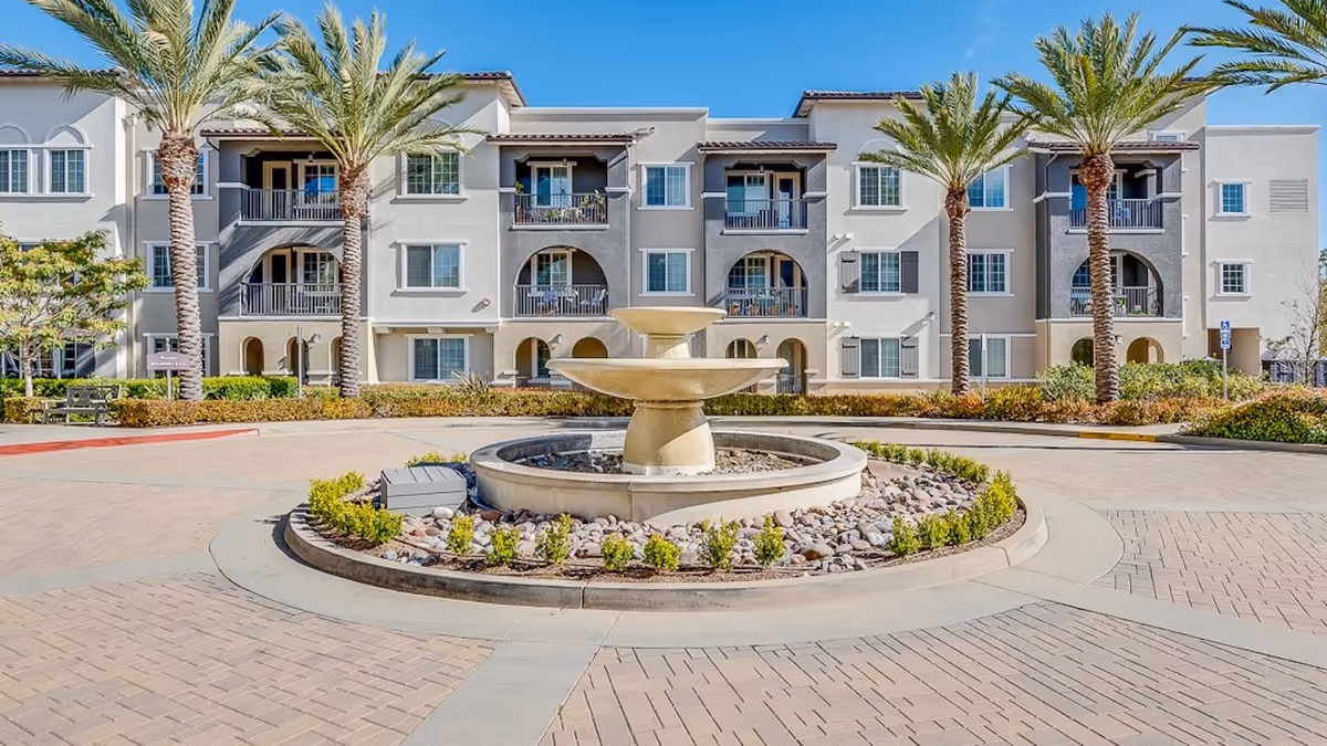 A senior living building with balconies, palm trees, and a central fountain.
