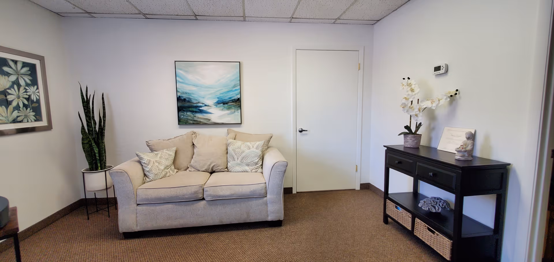 Cozy reception lounge at Fairway Medical with beige sofa, wall art, plants, and a dark console.
