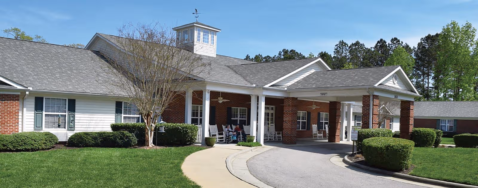 A senior living facility with brick exterior and a covered entrance surrounded by greenery.