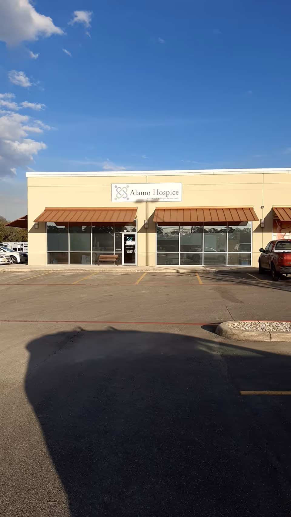 Alamo Hospice storefront with large glass windows and a parking lot.