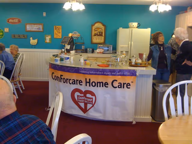 Interior at ComForCare Home Care with a coffee counter, teal wall, and people chatting.