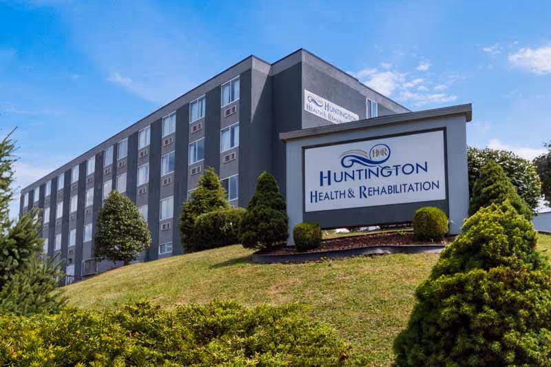 Exterior front view of the Huntington Health & Rehabilitation building with a large sign on a landscaped grassy slope.