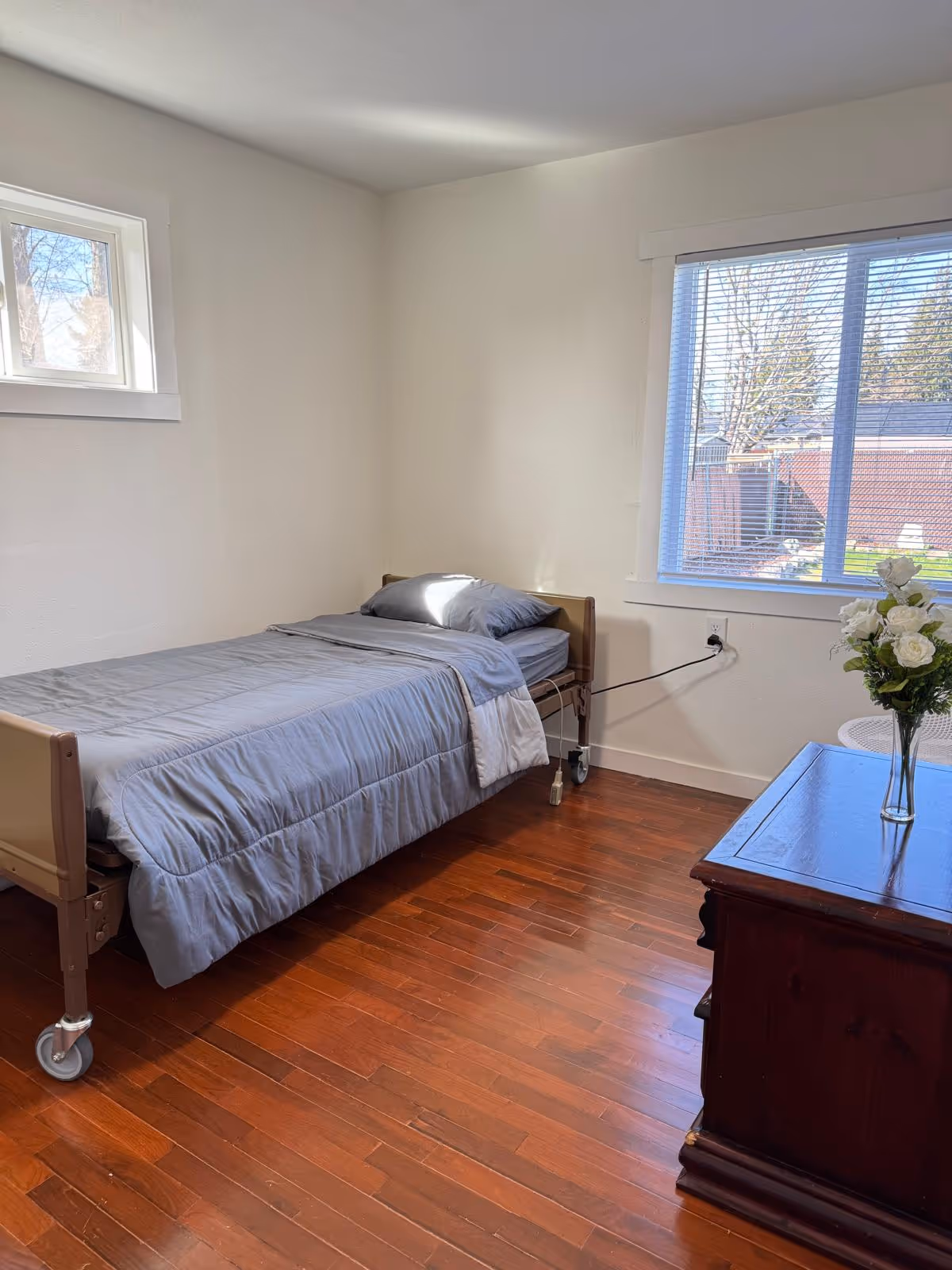 A small bedroom with a single hospital bed, wooden floor, and dresser.