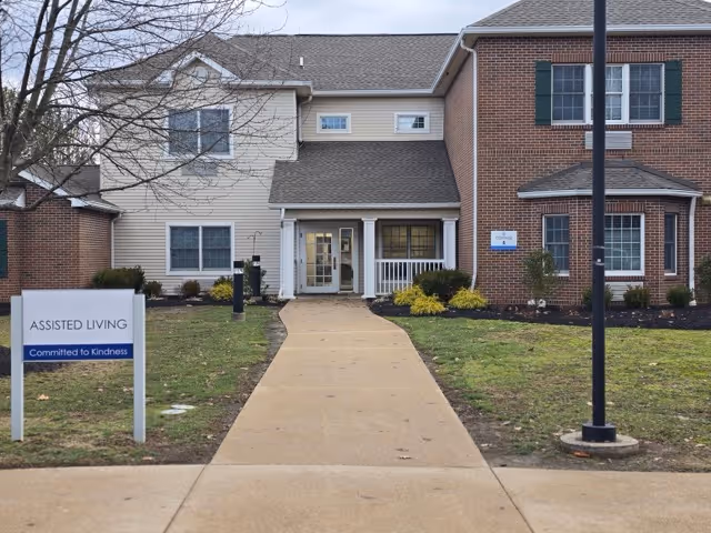 Front view of a two-story assisted living building with walkway, landscaping, and signage.